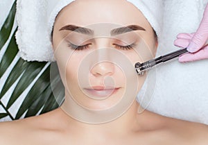 The cosmetologist makes the procedure Microdermabrasion of the facial skin of a beautiful, young woman in a beauty salon