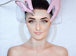 The cosmetologist makes the procedure Microdermabrasion of the facial skin of a beautiful, young woman in a beauty salon.