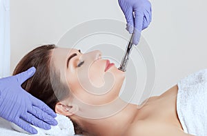 The cosmetologist makes the procedure Microdermabrasion of the facial skin of a beautiful, young woman in a beauty salon