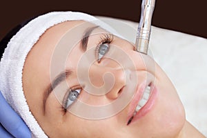 The cosmetologist makes the procedure Microdermabrasion of the facial skin of a beautiful, young woman in a beauty salon.