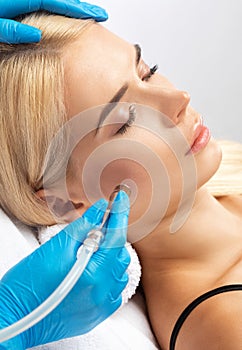 The cosmetologist makes the procedure Microdermabrasion of the facial skin of a beautiful, young woman in a beauty salon.