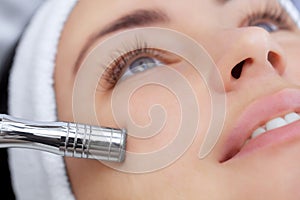 The cosmetologist makes the procedure Microdermabrasion of the facial skin of a beautiful, young woman photo