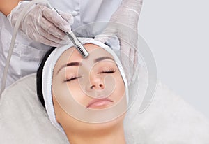 The cosmetologist makes the procedure Microdermabrasion of the facial skin of a beautiful, young woman photo