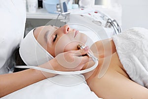The cosmetologist makes the procedure Microdermabrasion of the skin of the face of a beautiful, young woman in a beauty