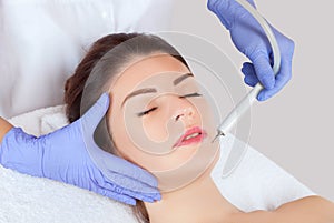 The cosmetologist makes the procedure treatment of Couperose and face cleaning of the skin of a beautiful, young woman in a beauty