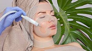 The cosmetologist makes the procedure treatment of Couperose and face cleaning of the skin of a beautiful, young woman in a beauty