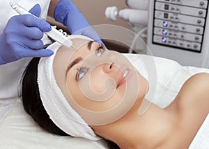 The cosmetologist makes the procedure treatment of Couperose of the facial skin of a beautiful, young woman in a beauty salon. photo