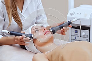 The cosmetologist makes the procedure an ultrasonic cleaning of the facial skin of a beautiful, young woman