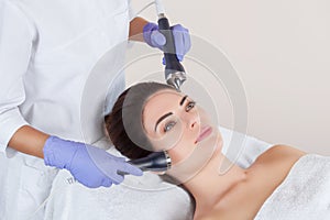 The cosmetologist makes the procedure an ultrasonic cleaning of the facial skin of a beautiful, young woman in a beauty salon