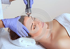 The cosmetologist makes the procedure an ultrasonic cleaning of the facial skin of a beautiful, young woman in a beauty salon