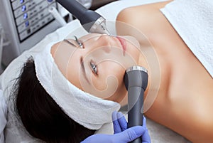 The cosmetologist makes the procedure an ultrasonic cleaning of the facial skin of a beautiful, young woman in a beauty salon