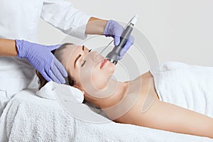 The cosmetologist makes the procedure an ultrasonic cleaning of the facial skin of a beautiful, young woman in a beauty salon.