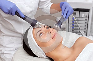 The cosmetologist makes the procedure an ultrasonic cleaning of the facial skin of a beautiful, young woman in a beauty salon.