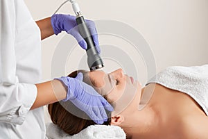 The cosmetologist makes the procedure an ultrasonic cleaning of the facial skin of a beautiful, young woman in a beauty salon.