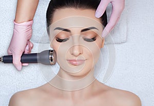 The cosmetologist makes the procedure an ultrasonic cleaning of the facial skin of a beautiful, young woman in a beauty salon