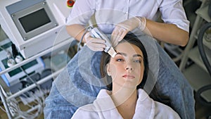 The cosmetologist makes the procedure ultrasonic face peeling of the facial skin of a beautiful, young woman in a beauty