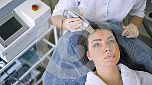 The cosmetologist makes the procedure ultrasonic face peeling of the facial skin of a beautiful, young woman in a beauty