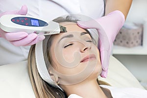 Cosmetologist makes an ultrasonic cleaning of the face of a young woman