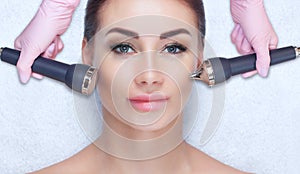 The cosmetologist makes the ultrasonic cleaning procedure of the facial skin of a beautiful woman in a beauty salon