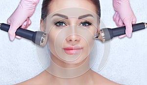 The cosmetologist makes the ultrasonic cleaning procedure of the facial skin of a beautiful woman in a beauty salon photo
