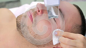 Cosmetologist makes ultrasonic face cleaning procedure to young man in clinic.