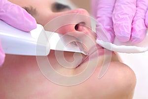 Cosmetologist makes ultrasonic face cleaning procedure to young woman in clinic.