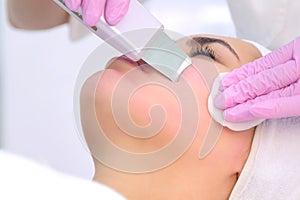 Cosmetologist makes ultrasonic face cleaning procedure to young woman in clinic.