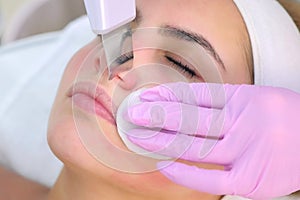 Cosmetologist makes ultrasonic face cleaning procedure to young woman in clinic.