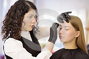 Cosmetologist making eyebrows makeup. Attractive woman getting facial care at beauty salon. Architecture eyebrows