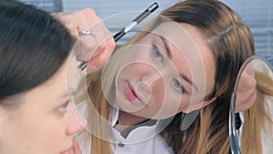 Cosmetologist making tint eyebrows procedure to young woman in beauty clinic.