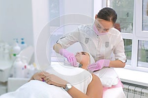 Cosmetologist making ultrasonic face cleaning procedure to woman in clinic.