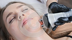 Cosmetologist moves RF applicator across woman face