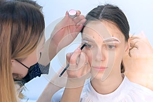 Cosmetologist painting brush shape of eyebrows woman before tint procedure.