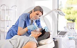 Cosmetologist performing female face skin massage procedure in cosmetology clinic