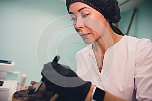 The cosmetologist in pink gloves with a brush applies a carbon mask for peeling on the face of a young girl in a