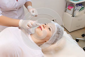 Cosmetologist prepares the client`s lips for the augmentation procedure