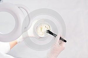 Cosmetologist prepares a rejuvenating mask in a bawl for face procedure wearing white protective gloves.