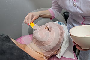 The cosmetologist for procedure of cleansing and moisturizing the skin, applying a Alginic mask to the face of a young woman in