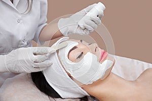 The cosmetologist for procedure of cleansing and moisturizing the skin, applying a Alginic mask to the face of a young woman in be