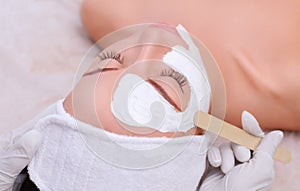 The cosmetologist for the procedure of cleansing and moisturizing the skin, applying a mask with stick to the face