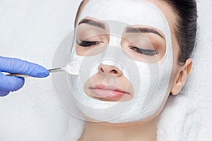 The cosmetologist for the procedure of cleansing and moisturizing the skin, applying a mask with stick to the face