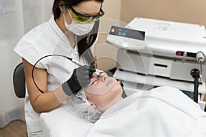 Cosmetologist in protective glasses conducts laser treatment of the skin for a young patient in a cosmetology clinic
