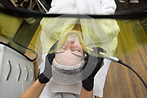 Cosmetologist in protective glasses conducts laser treatment of the skin for a young patient in a cosmetology clinic