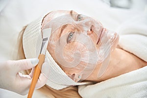 Cosmetologist in protective gloves applying collagen face mask to woman