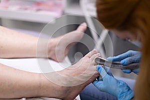 The cosmetologist removes keratinized skin from the feet with pliers.
