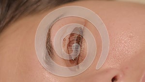 Cosmetologist is removing excess of paint during laminating eye lashes of caucasian brunette lady. Top view extreme
