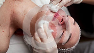 Cosmetologist removing facial mask from female face with napkin. Beautician make facial treatment to woman in medical