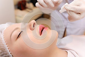 Cosmetologist rubs the girl`s lips with oil for care after the lip augmentation procedure with hyaluronic acid