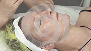 Cosmetologist smear humidify oil on adult woman face by hands in beauty saloon.