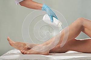 Cosmetologist is sprinkling and distributing talcum powder on a young girl`s leg before the epilation procedure.